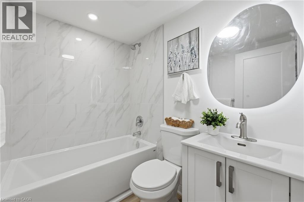 White tile surround with subtle veining, recessed lighting, built-in bathtub, white vanity with integrated sink, and illuminated oval mirror - 156 East 36Th Street, Hamilton, ON - Indoor Photo Showing Bathroom