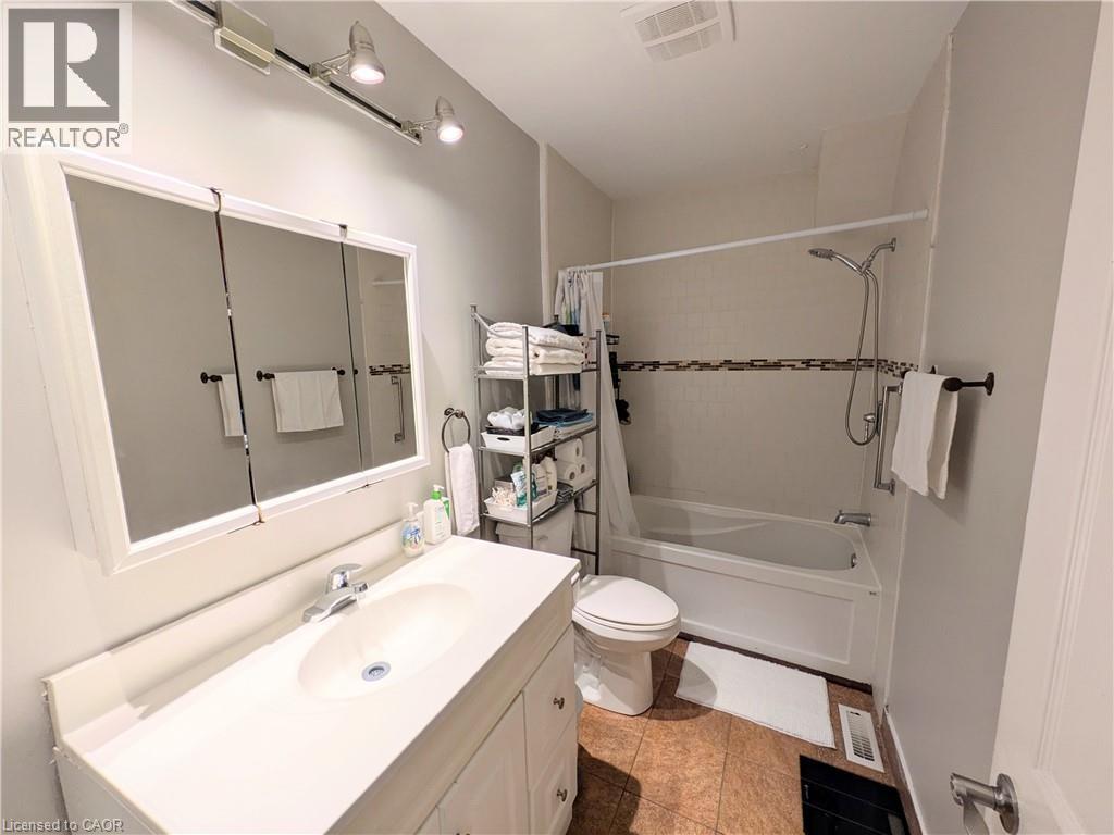 Bathroom featuring a white vanity with integrated sink, tri-panel mirrored medicine cabinet, track lighting, and a bathtub with a tiled surround - 7 Campbell Avenue, Hamilton, ON - Indoor Photo Showing Bathroom