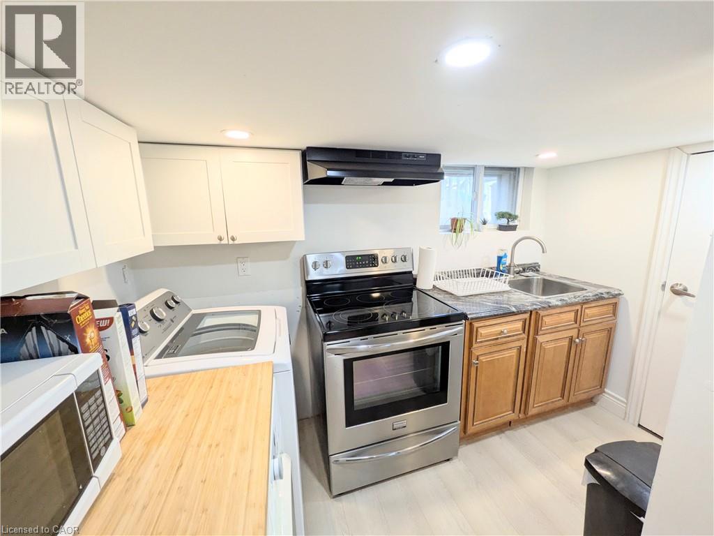 Compact kitchen area featuring stainless steel appliances, light wood-finish flooring, white upper cabinetry, and a dark stone-finish countertop with an integrated sink - 7 Campbell Avenue, Hamilton, ON - Indoor