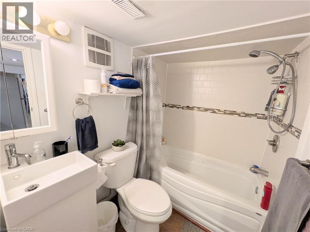 Full bath featuring a white vanity with an integrated rectangular sink, wall-mounted mirror, and a combination shower and tub with subway tile surround and decorative accent band - 7 Campbell Avenue, Hamilton, ON - Indoor Photo Showing Bathroom
