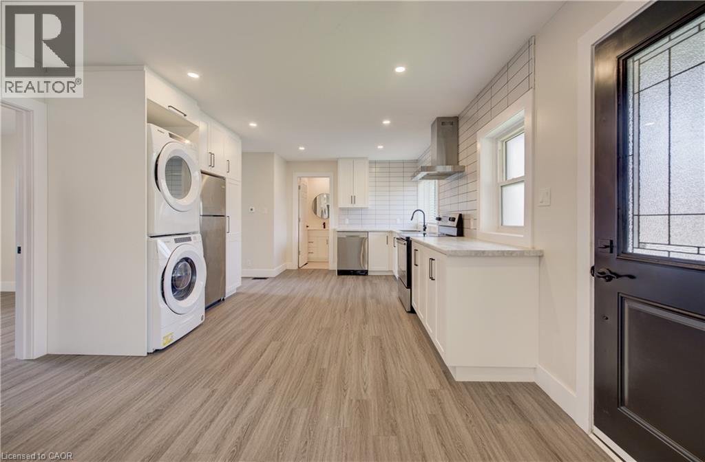 Open-concept kitchen featuring wood-finish flooring, white cabinetry with contemporary hardware, light-toned countertops, and a white subway tile backsplash - 361 Prospect Avenue, Kitchener, ON - Indoor Photo Showing Laundry Room