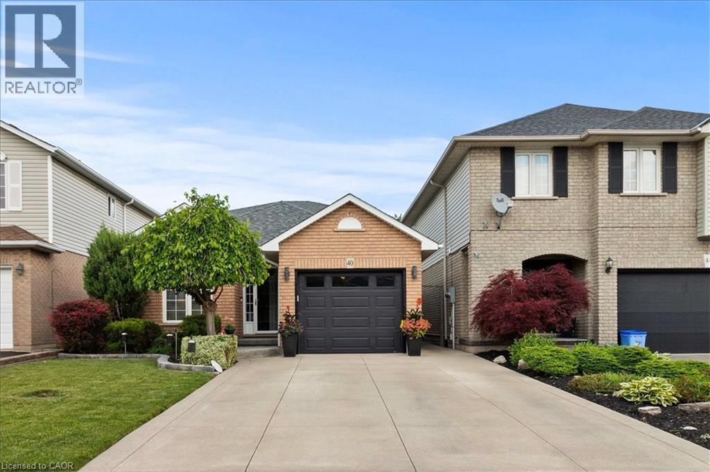 Brick facade residence featuring a single-car garage with a dark gray door, a concrete driveway, and established front landscaping - 40 Bridgette Drive, Hamilton, ON - Outdoor With Facade