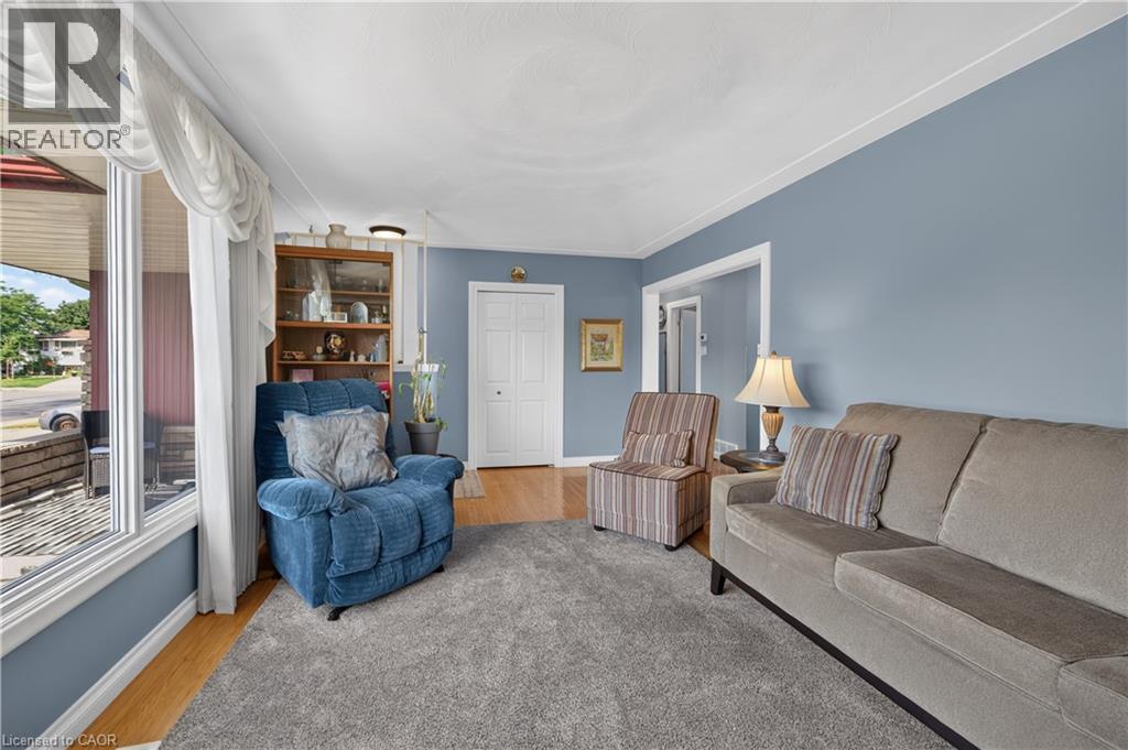 Expansive window providing ample natural light, light blue wall paint, white trim, wood-finish flooring, and a built-in display cabinet - 5 Kentley Drive, Hamilton, ON - Indoor Photo Showing Living Room