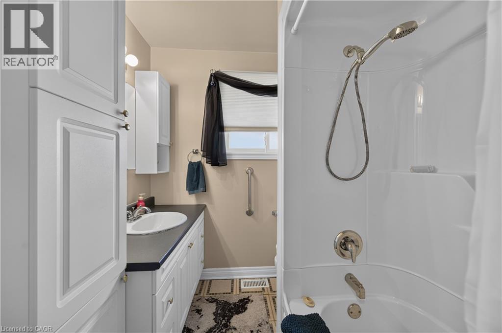 White cabinetry, built-in storage tower, dark countertop, white drop-in sink, and a white tub with an integrated shower - 5 Kentley Drive, Hamilton, ON - Indoor Photo Showing Bathroom