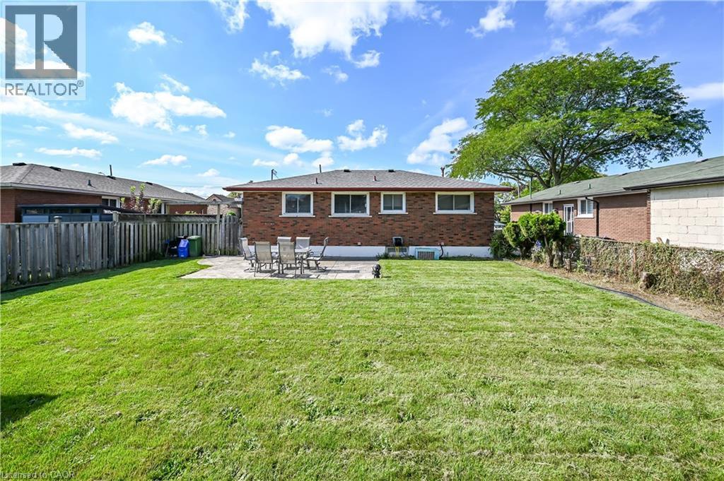 Expansive backyard with a manicured lawn, brick exterior, and a stone patio - 5 Kentley Drive, Hamilton, ON - Outdoor