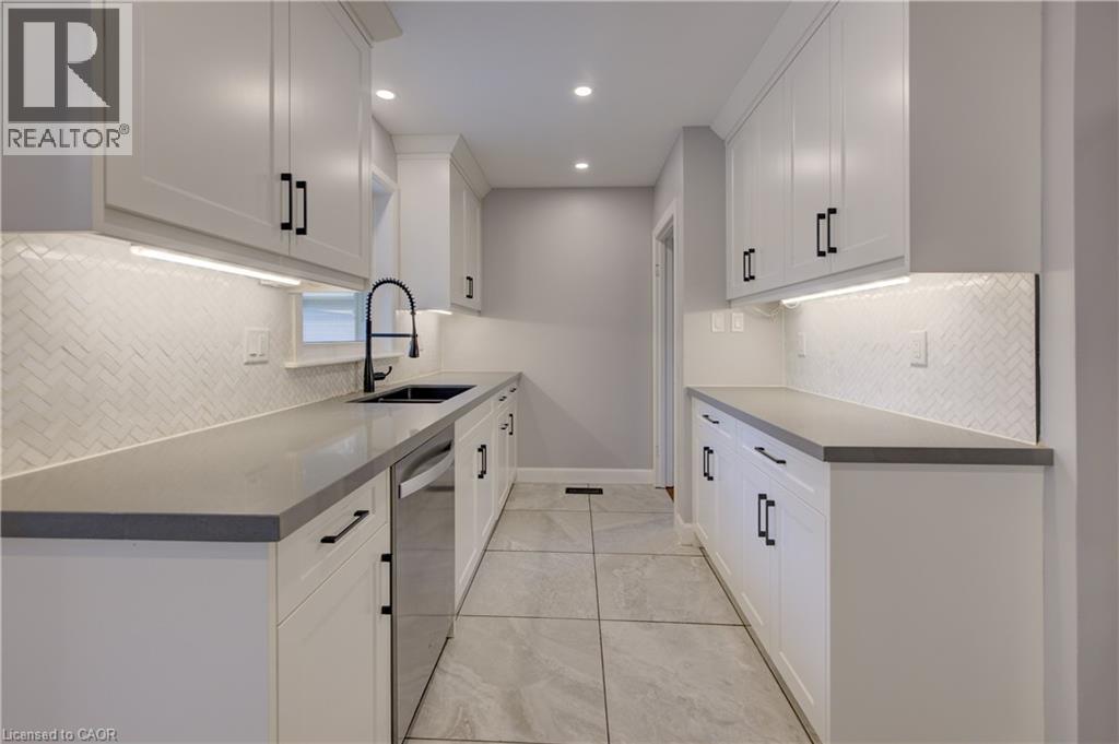 White shaker cabinetry with matte black hardware, grey countertops, herringbone tile backsplash, recessed lighting, and a stainless steel dishwasher - 244 Royal Street, Waterloo, ON - Indoor Photo Showing Kitchen With Upgraded Kitchen