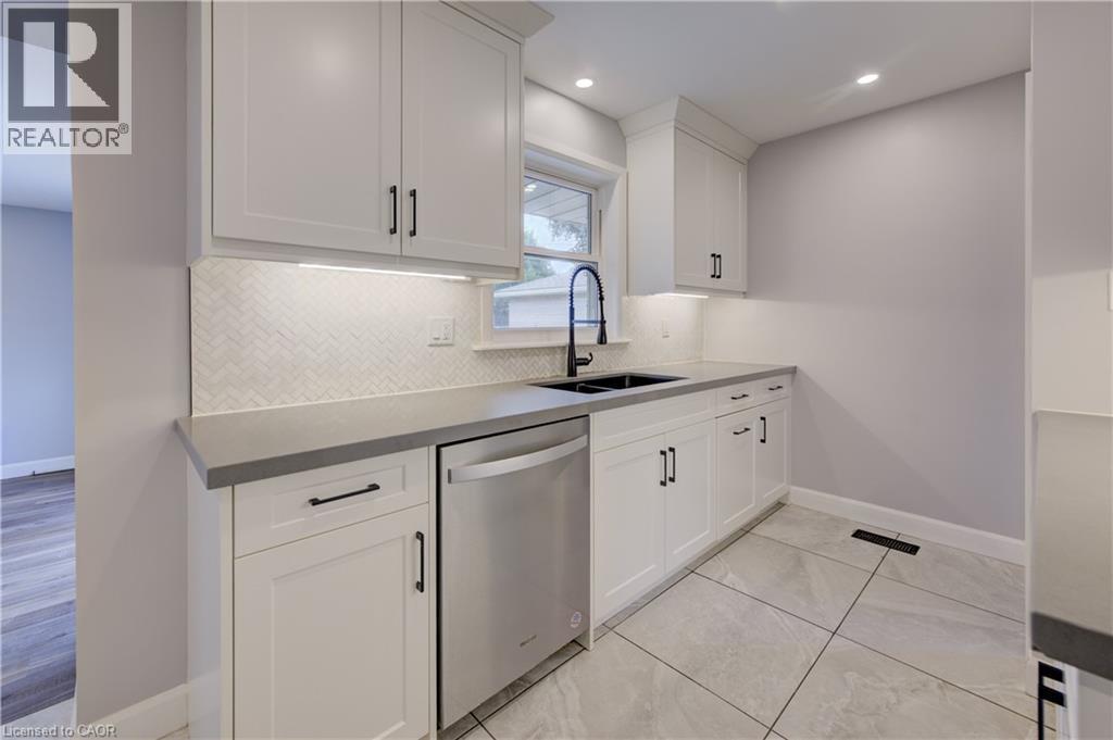 White shaker cabinetry, herringbone tile backsplash, under-cabinet lighting, dark countertop, and large format tile flooring - 244 Royal Street, Waterloo, ON - Indoor Photo Showing Kitchen With Double Sink