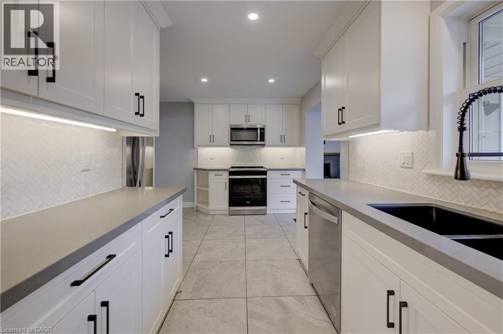 Galley kitchen featuring white cabinetry, light gray countertops, stainless steel appliances, and a herringbone tile backsplash - 244 Royal Street, Waterloo, ON - Indoor Photo Showing Kitchen With Double Sink
