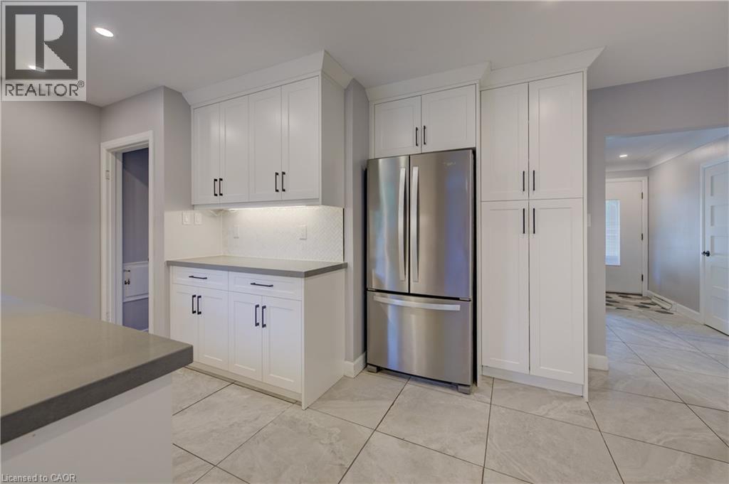 White shaker cabinetry, stainless steel French door refrigerator, light gray countertops, white geometric tile backsplash, and light gray tile flooring - 244 Royal Street, Waterloo, ON - Indoor Photo Showing Kitchen