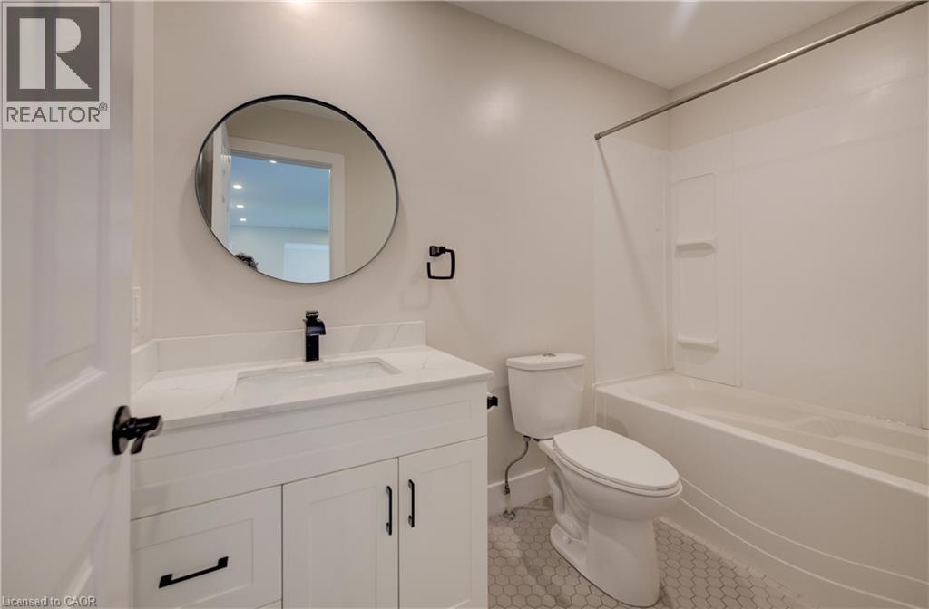 Bathroom featuring a white vanity with integrated sink, a dark finish single-handle faucet, and a round wall-mounted mirror - 361 Prospect Avenue, Kitchener, ON - Indoor Photo Showing Bathroom