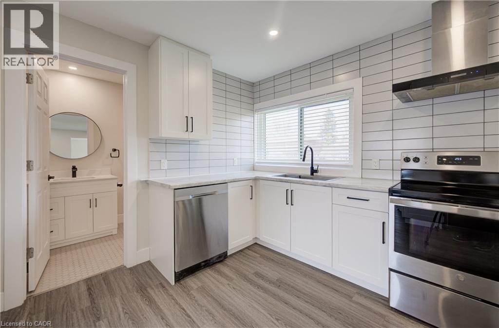 Modern kitchen featuring white shaker-style cabinetry, stainless steel appliances including a dishwasher and range with a matching vent hood, and wood-finish flooring - 361 Prospect Avenue, Kitchener, ON - Indoor Photo Showing Kitchen