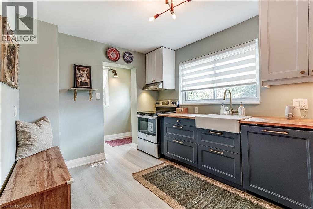 Kitchen featuring light wood-finish flooring, white upper cabinetry, dark lower cabinetry, wood countertops, and a white farmhouse sink with a gooseneck faucet - 2488 Brookhurst Road, Mississauga, ON - Indoor Photo Showing Kitchen