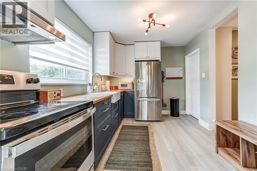 Kitchen featuring light wood-finish flooring, two-tone cabinetry, a farmhouse-style sink, and stainless steel appliances - 2488 Brookhurst Road, Mississauga, ON - Indoor Photo Showing Kitchen