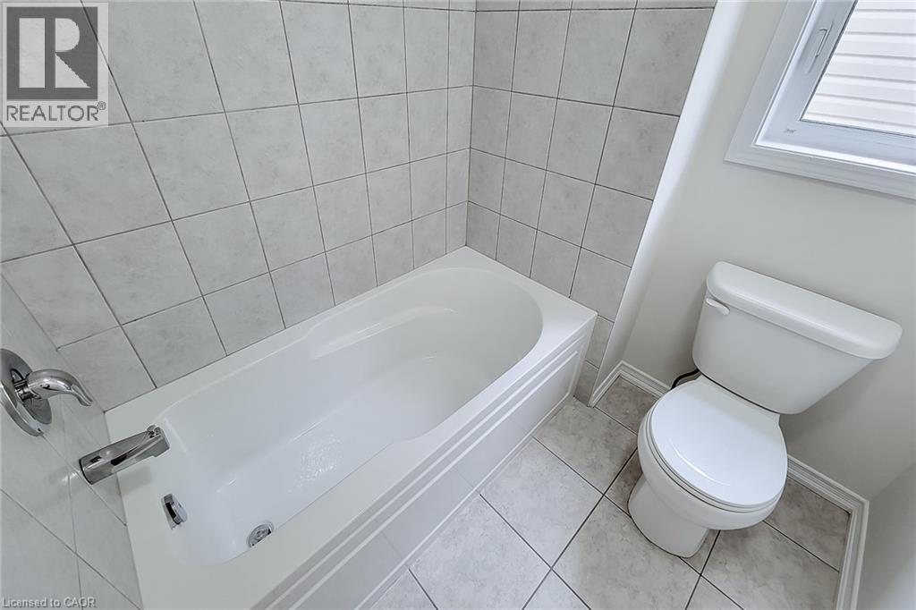 White ceramic tile flooring and wall surround, a white bathtub with chrome fixtures, and a white toilet - 11 Esther Crescent, Thorold, ON - Indoor Photo Showing Bathroom