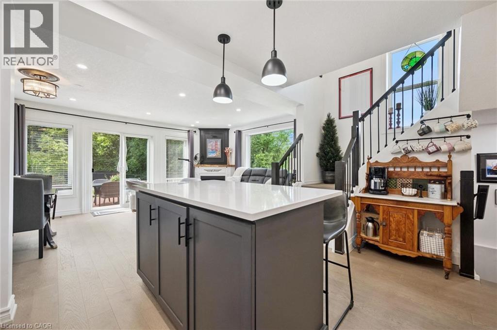 Central island with a light-toned countertop, wood-finish flooring, sliding glass patio doors, built-in fireplace, and a staircase with an iron railing - 439 Beaver Creek Road, Waterloo, ON - Indoor Photo Showing Kitchen