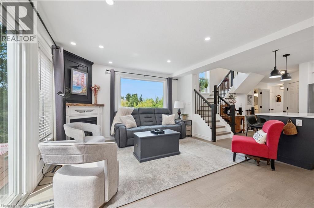 Recessed ceiling lighting, wood-finish flooring, built-in fireplace with mantel, staircase with dark wood-finish handrail and black balusters, and a built-in kitchen island with pendant lighting - 439 Beaver Creek Road, Waterloo, ON - Indoor Photo Showing Living Room