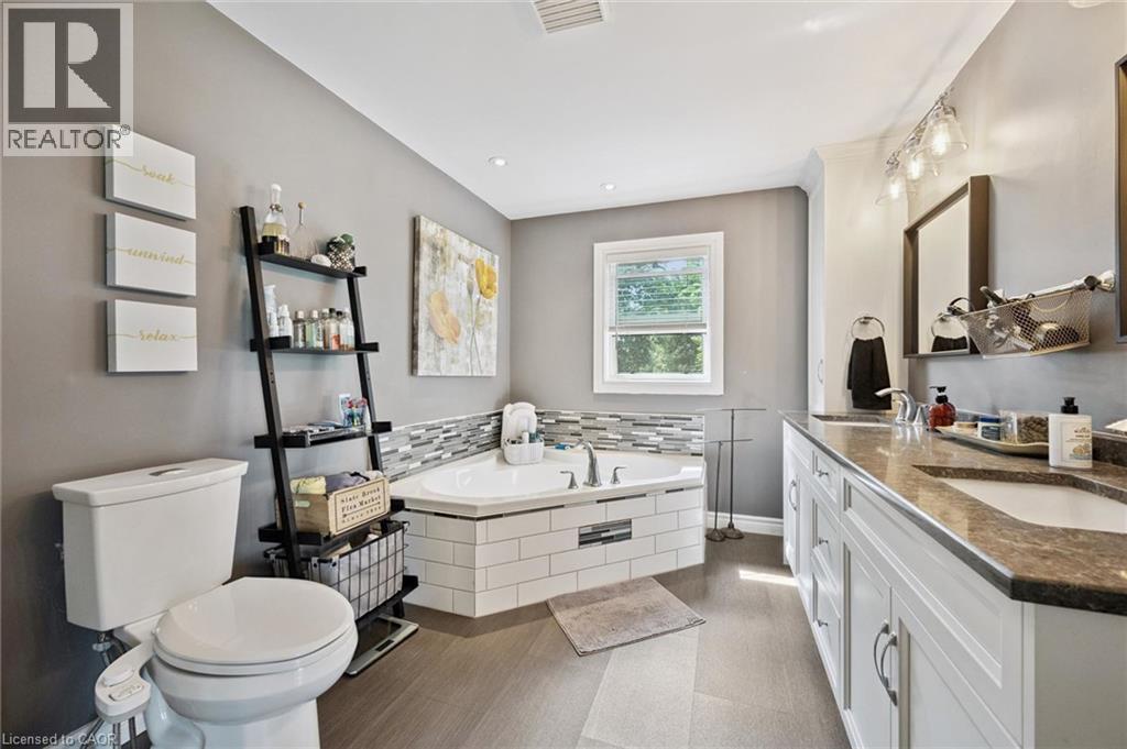 Corner soaking tub with mosaic tile surround, wood-finish flooring, dual vanity with undermount sinks, and a window providing natural light - 439 Beaver Creek Road, Waterloo, ON - Indoor Photo Showing Bathroom
