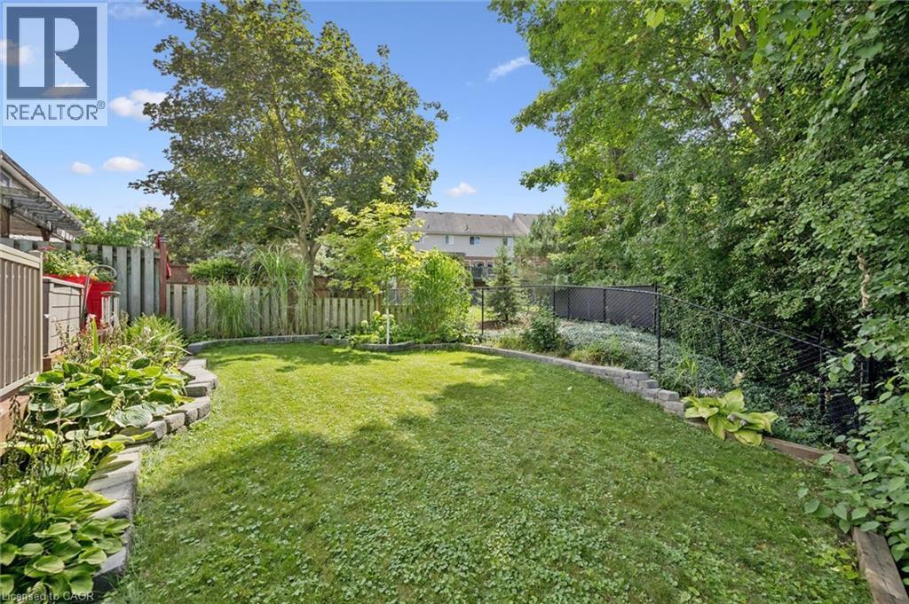 Expansive backyard featuring a manicured lawn, tiered landscaping with stone block retaining walls, mature trees, and privacy fencing - 439 Beaver Creek Road, Waterloo, ON - Outdoor