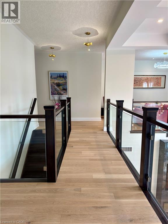 Hardwood flooring, dark wood newel posts, glass railings, and modern pendant lighting - 923 Eaglecrest Court, Kitchener, ON - Indoor Photo Showing Other Room