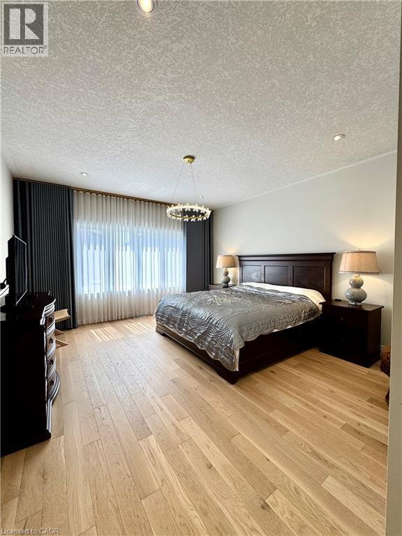Hardwood flooring, recessed ceiling lighting, decorative chandelier, dark wood-finish bed frame, and large window with privacy sheers - 923 Eaglecrest Court, Kitchener, ON - Indoor Photo Showing Bedroom