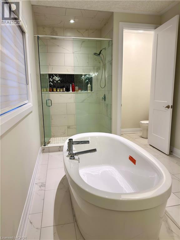 Freestanding soaking tub with chrome fixtures, glass-enclosed shower with tile surround, built-in shower niche with herringbone tile accent, and large format tile flooring - 923 Eaglecrest Court, Kitchener, ON - Indoor Photo Showing Bathroom