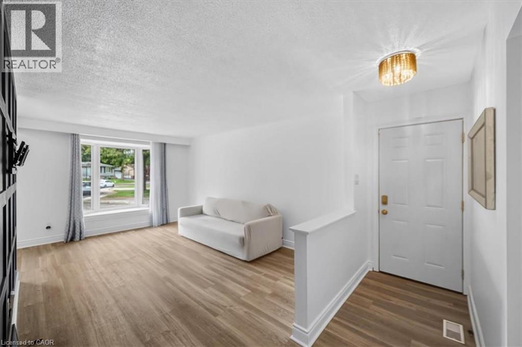 Expansive living area featuring light wood-finish flooring, a large bay window, and a contemporary ceiling fixture - 27 Gretna Court, Hamilton, ON - Indoor