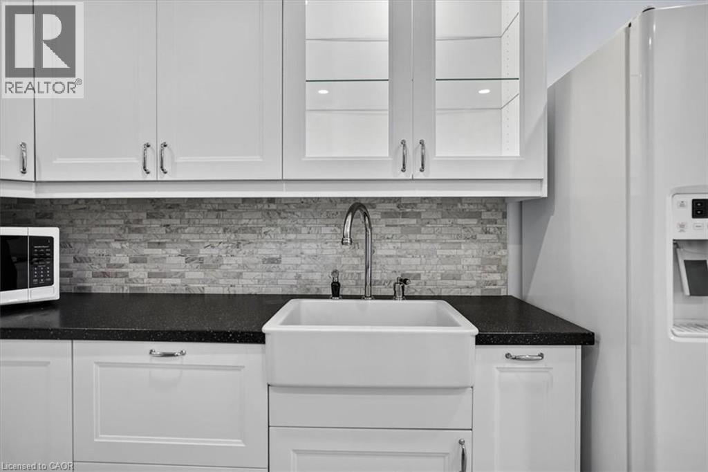 White shaker-style cabinetry with chrome hardware, dark speckled countertops, subway tile backsplash, and a farmhouse-style sink - 27 Gretna Court, Hamilton, ON - Indoor Photo Showing Kitchen With Double Sink With Upgraded Kitchen