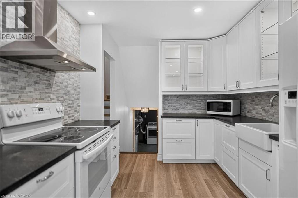 Kitchen featuring white shaker-style cabinetry, dark countertops, a mosaic tile backsplash, wood-finish flooring, and a farmhouse-style sink - 27 Gretna Court, Hamilton, ON - Indoor Photo Showing Kitchen