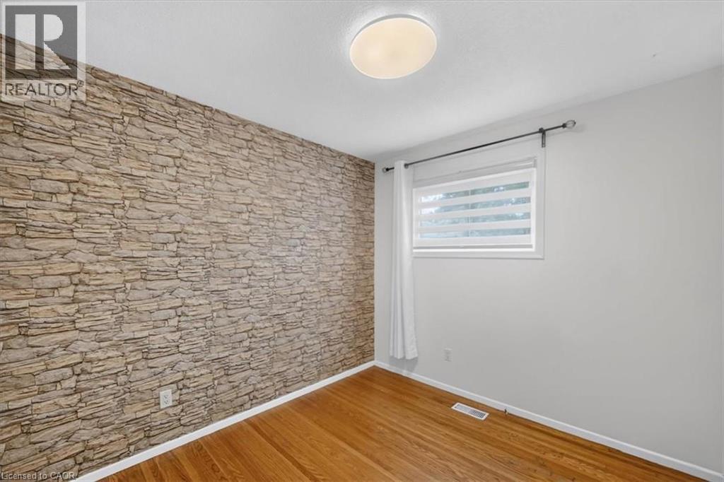Stone-finish accent wall, wood-finish flooring, and a flush-mount ceiling light - 27 Gretna Court, Hamilton, ON - Indoor Photo Showing Other Room