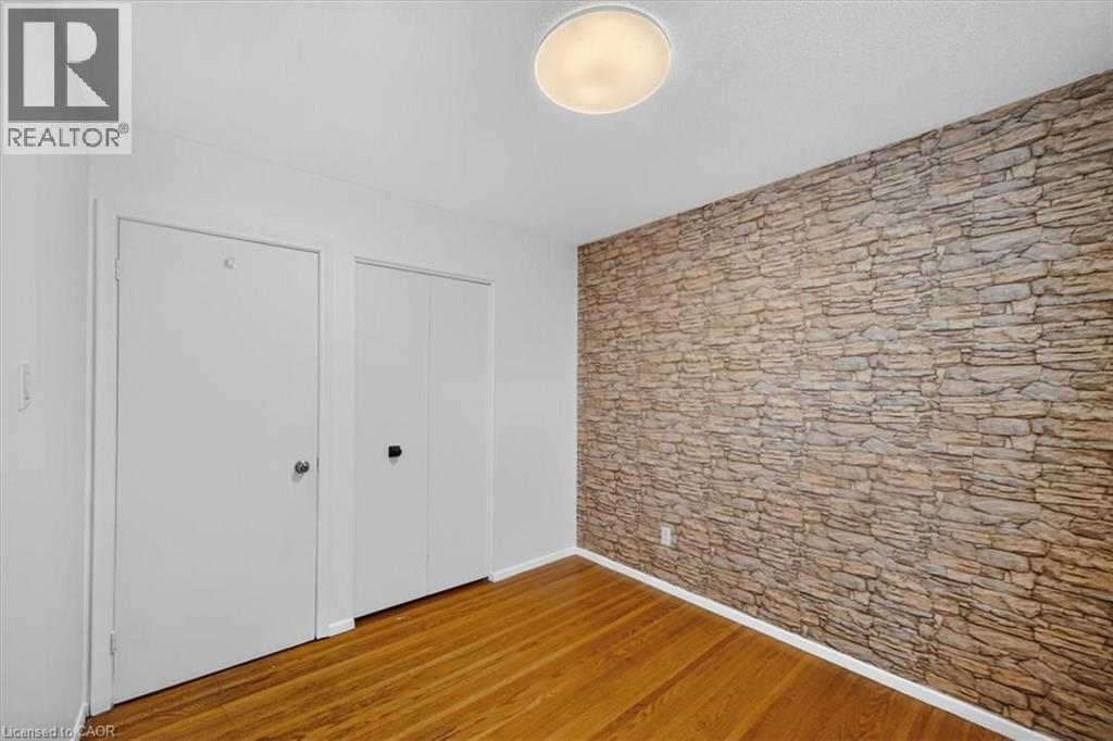 Hardwood flooring and a stone-effect accent wall - 27 Gretna Court, Hamilton, ON - Indoor Photo Showing Other Room