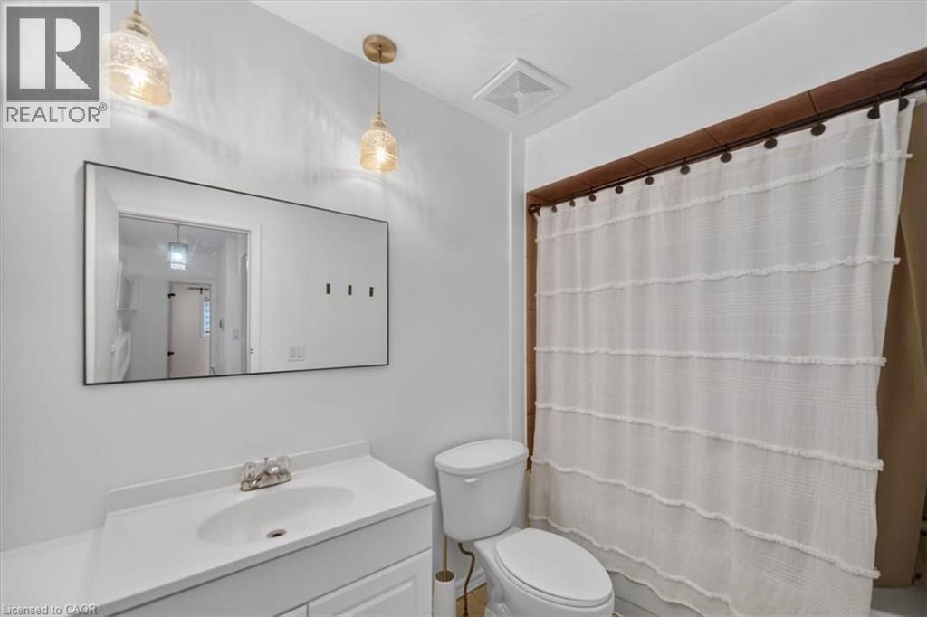 Vanity with integrated sink and chrome-finish faucet, rectangular framed mirror, and two pendant light fixtures - 27 Gretna Court, Hamilton, ON - Indoor Photo Showing Bathroom