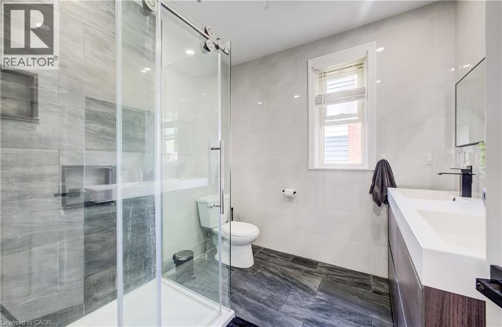 Full glass shower enclosure with sliding door, built-in shower niche, floating vanity with integrated sink, contemporary black faucet, and tiled walls and flooring - 34 St Clair Avenue, Kitchener, ON - Indoor Photo Showing Bathroom
