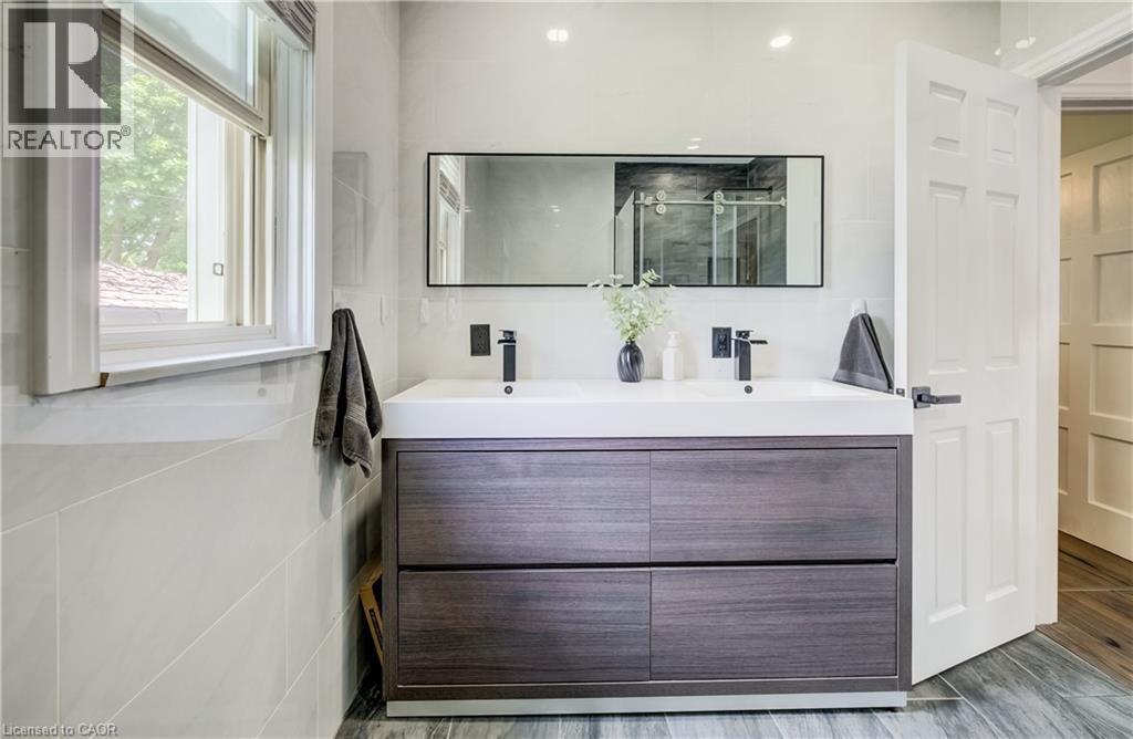 Dual sink vanity with wood-finish cabinetry, matte black fixtures, and a framed mirror - 34 St Clair Avenue, Kitchener, ON - Indoor Photo Showing Bathroom