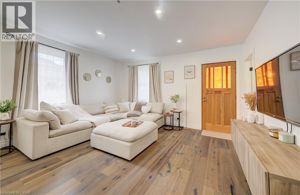 Wood-finish flooring throughout, recessed ceiling lighting, natural wood front entry door with glass paneling, and an integrated wood-finish entertainment console - 34 St Clair Avenue, Kitchener, ON - Indoor Photo Showing Living Room