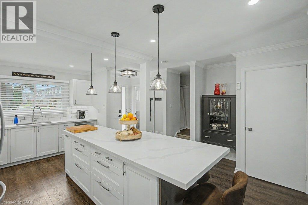 Spacious kitchen featuring a large central island with a solid surface countertop, white cabinetry with contemporary hardware, wood-finish flooring, and pendant lighting - 2050 Upper Middle Road Unit# 164, Burlington, ON - Indoor Photo Showing Kitchen With Upgraded Kitchen