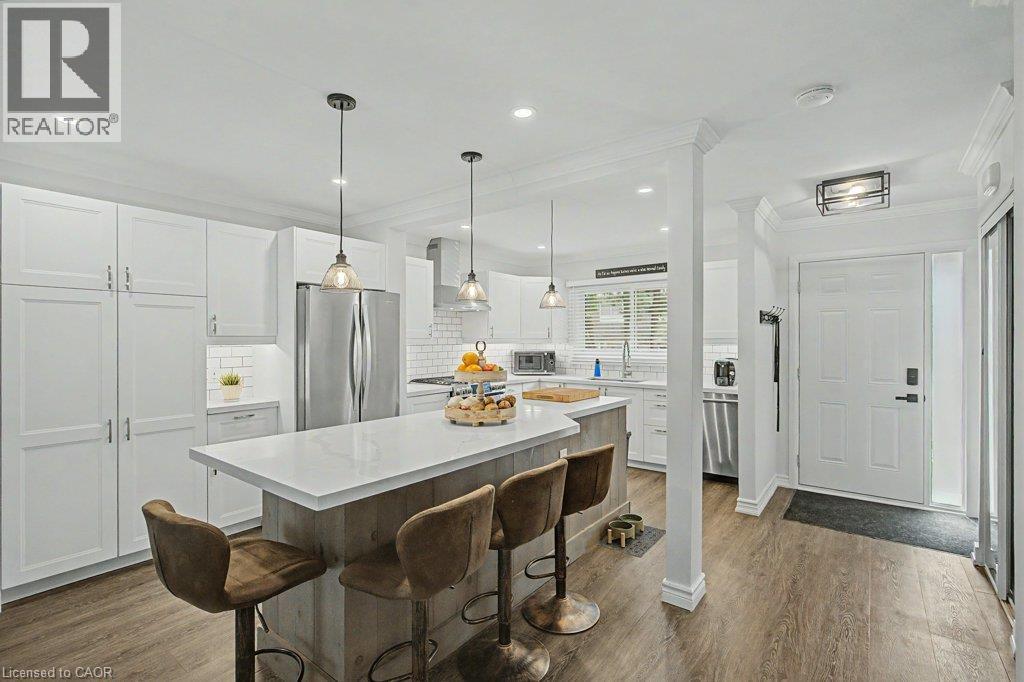 Modern kitchen featuring white shaker cabinetry, stainless steel appliances, a center island with counter seating, quartz countertops, and wood-finish flooring - 2050 Upper Middle Road Unit# 164, Burlington, ON - Indoor Photo Showing Kitchen With Upgraded Kitchen