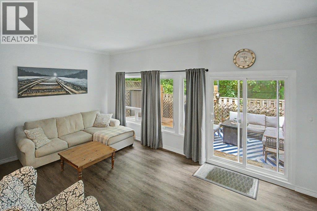 Wood-finish flooring throughout, a large sliding glass door opening to an outdoor patio, multiple windows for natural light, and crown molding - 2050 Upper Middle Road Unit# 164, Burlington, ON - Indoor Photo Showing Living Room