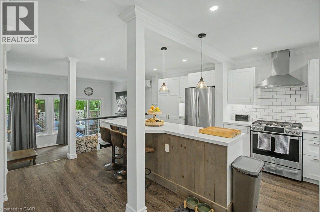Kitchen featuring wood-finish flooring, white cabinetry, subway tile backsplash, stainless steel appliances, and a breakfast bar with paneling - 2050 Upper Middle Road Unit# 164, Burlington, ON - Indoor Photo Showing Kitchen With Upgraded Kitchen