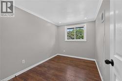 Wood-finish flooring with white baseboards, a white-framed window, recessed ceiling lighting, and crown molding -