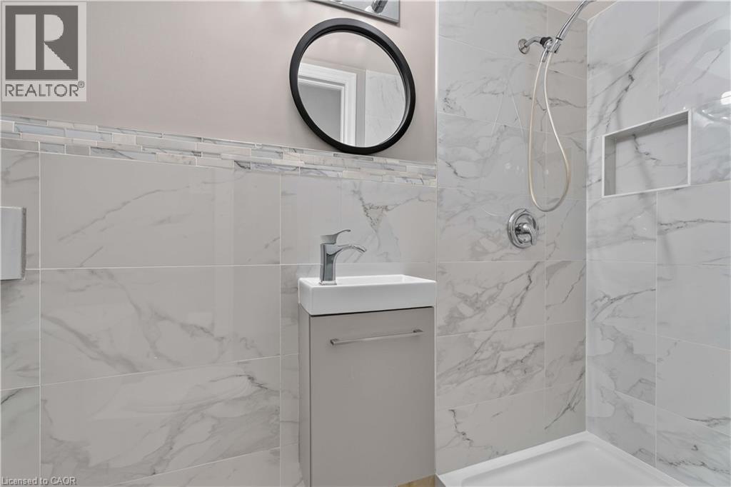 Shower with large format porcelain tile, mosaic accent border, built-in shower niche, and wall-mounted vanity with integrated sink - 66 Summercrest Drive Unit# 3, Hamilton, ON - Indoor Photo Showing Bathroom