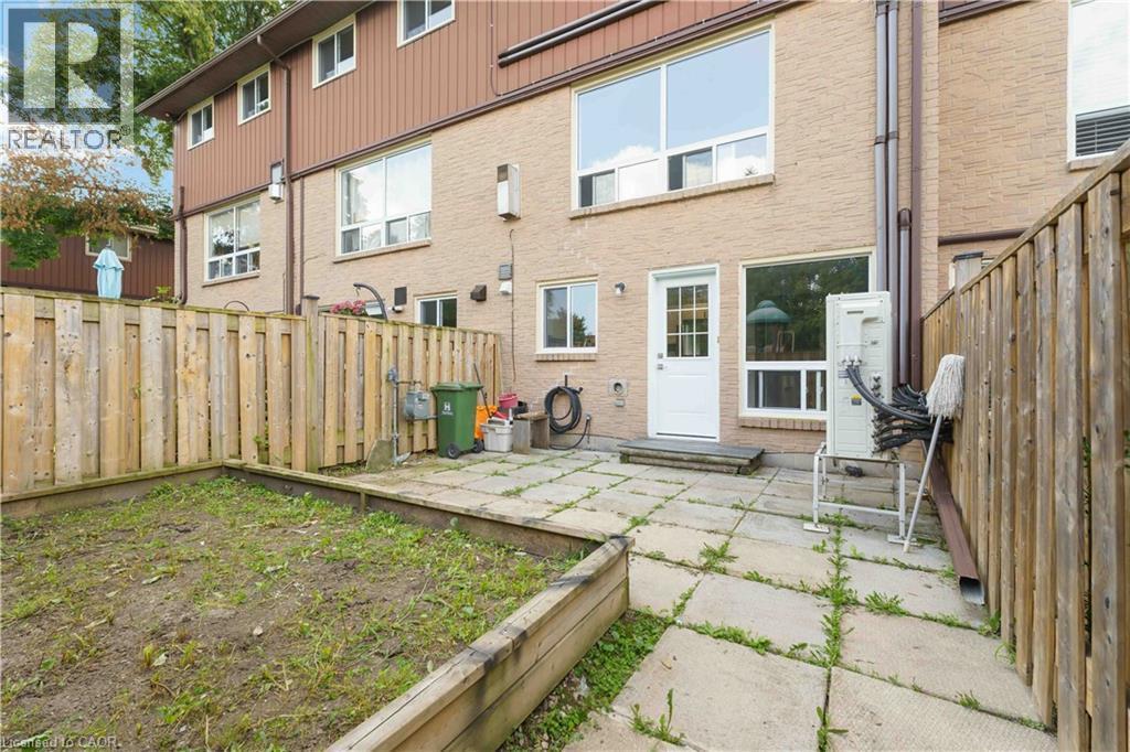 Rear exterior featuring a brick facade, white door with glass panels, large windows, and a paved patio area - 66 Summercrest Drive Unit# 3, Hamilton, ON - Outdoor With Exterior