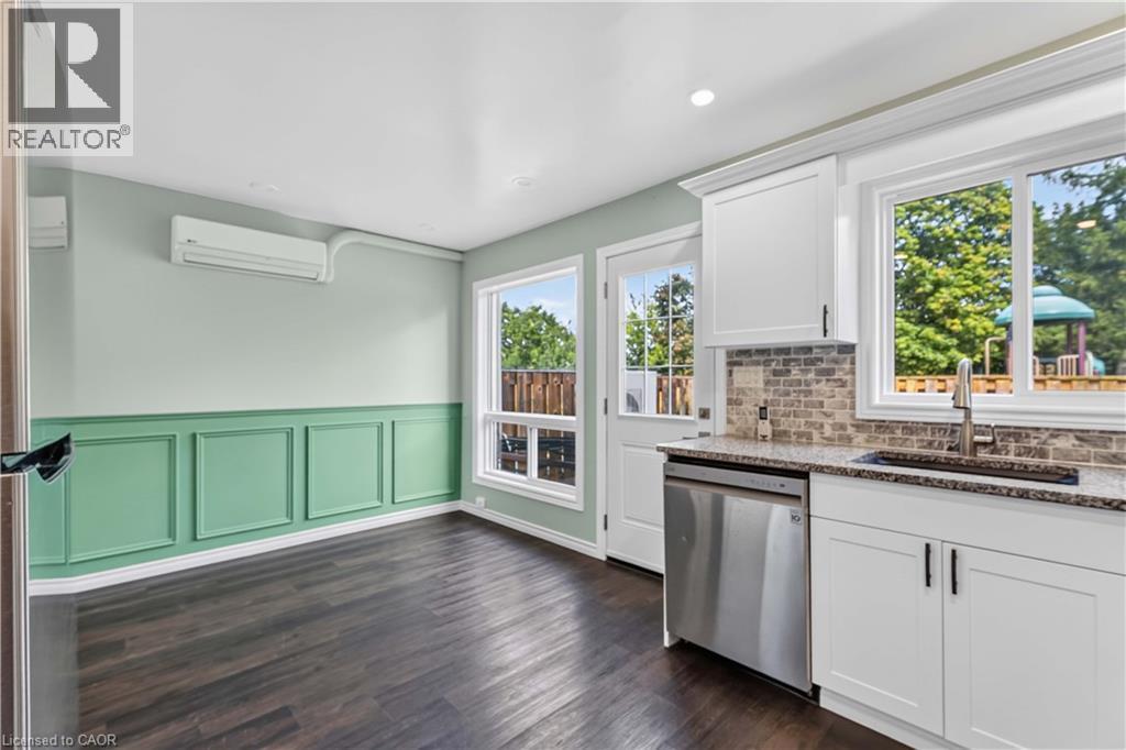 Dark wood-finish flooring, accent wall with decorative molding, white cabinetry, granite countertop, and stainless steel dishwasher - 66 Summercrest Drive Unit# 3, Hamilton, ON - Indoor Photo Showing Kitchen