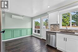 Dark wood-finish flooring, accent wall with decorative molding, white cabinetry, granite countertop, and stainless steel dishwasher -