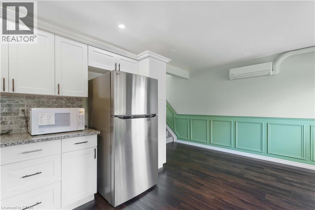 White cabinetry, granite-look countertop, tile backsplash, dark wood-finish flooring, and decorative wainscoting - 66 Summercrest Drive Unit# 3, Hamilton, ON - Indoor Photo Showing Kitchen