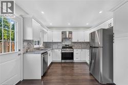 White shaker cabinetry, stainless steel appliances, granite countertops, tile backsplash, and dark wood-finish flooring -