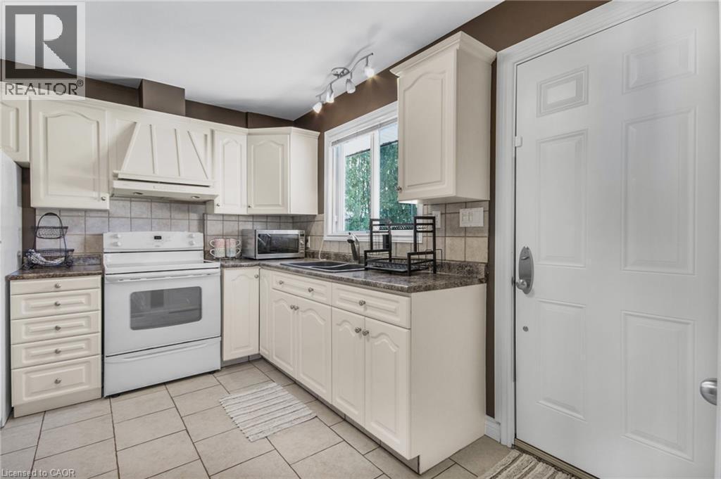 Light-toned cabinetry with decorative molding, solid surface countertops, tiled flooring, built-in range hood, and a window with natural light - 185 Burlington Street, London, ON - Indoor Photo Showing Kitchen With Double Sink