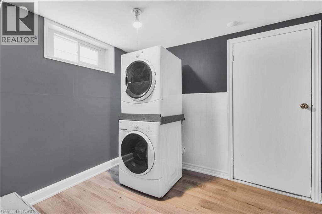 Stackable laundry appliances with a wood-finish floor and white trim - 185 Burlington Street, London, ON - Indoor Photo Showing Laundry Room