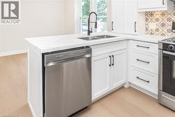 White cabinetry with matte black hardware, stainless steel dishwasher, double basin sink with a gooseneck faucet, light wood-finish flooring, and a patterned tile backsplash - 