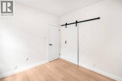 Light-toned wood-finish flooring, white walls, and a modern barn door with black hardware - 
