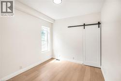White barn door with matte black hardware, wood-finish flooring, recessed lighting, and a single pane window - 